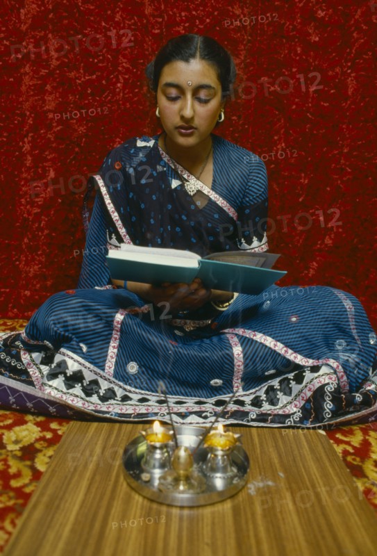 SOCIETY, Religion, Hinduism, England.  Girl reading Holy book in front of lighted candles and incense during Dirwali.