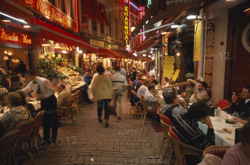 BELGIUM, Brabant, Brussels, People sitting at outside tables in narrow street lined with restaurants at night.