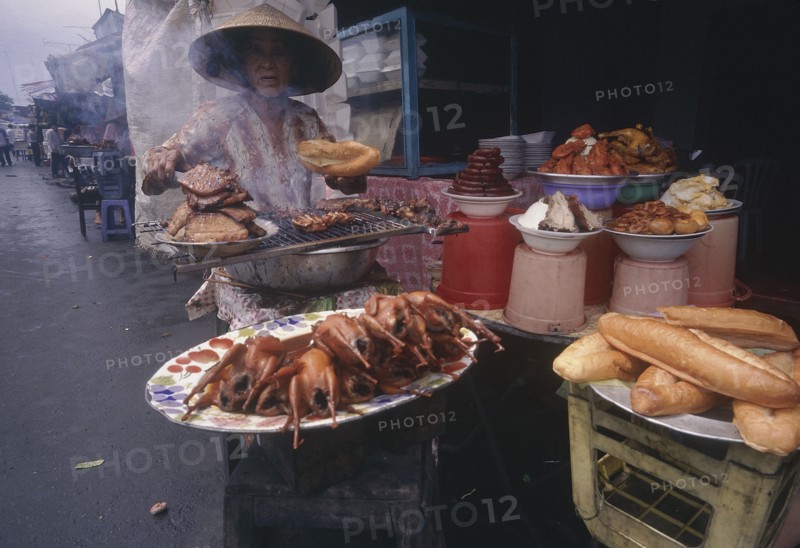 VIETNAM, Mekong Delta, Vinh Long, Woman cooking various meat products at market stall.