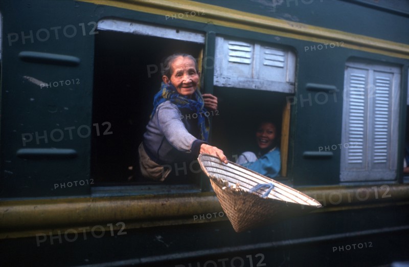 VIETNAM, Hai Van Pass, Old woman reaching out of the window of a train carriage with a straw hat in her outstretched hand.