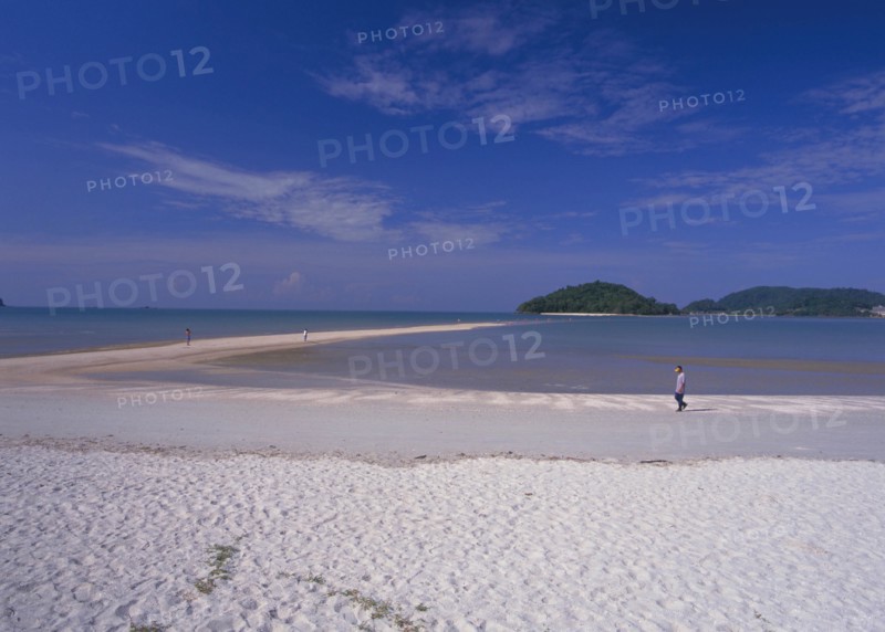 MALAYSIA, Langkawi, Kedah, Pantai Cenang beach with man walking near the the sand bar at low tide to Pulau Rebak Kecil island