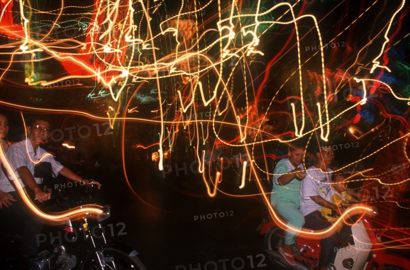 VIETNAM, Ho Chi Minh City, Motor cycle riders on the evening of Liberation Day and coloured light trails.