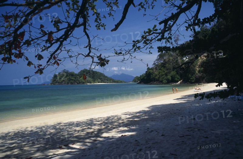 MALAYSIA, Kedah, Langkawi, Datai Bay beach with tourists walking by the water’s edge looking out to sea