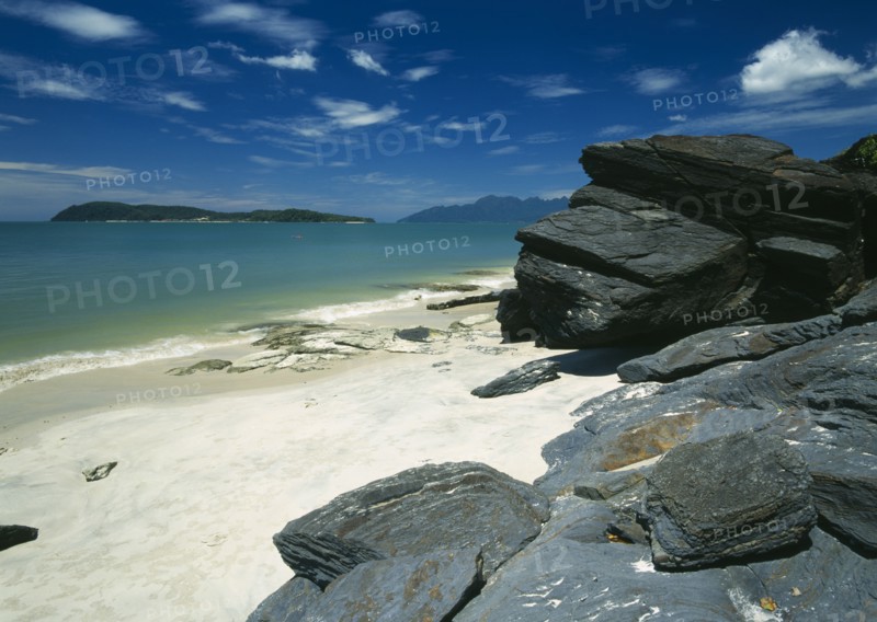 MALAYSIA, Kedah, Langkawi, Pantai Tengah beach looking towards Pulau Rebak Besar island with rocks in the foreground