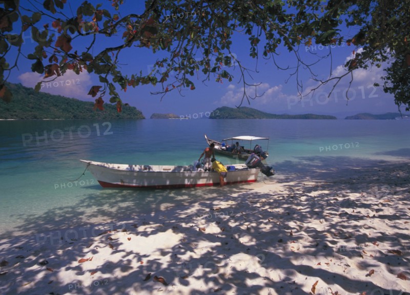 MALAYSIA, Kedah, Langkawi, Pulau Singa Besar wildlife reserve island with men unloading long boats under the shade of the trees