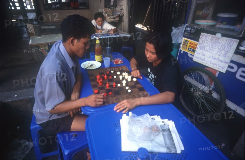 THAILAND, Bangkok, Couple playing a board game at a streetside cafe.