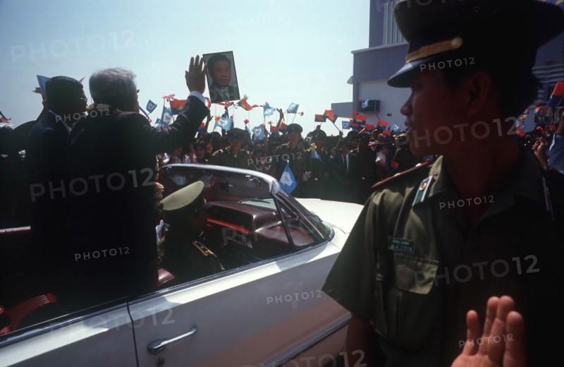 CAMBODIA, Phnom Pehn, Sihanouk and Hun Sen leave Pochentong airport in an open top car past waving crowds and soldiers.