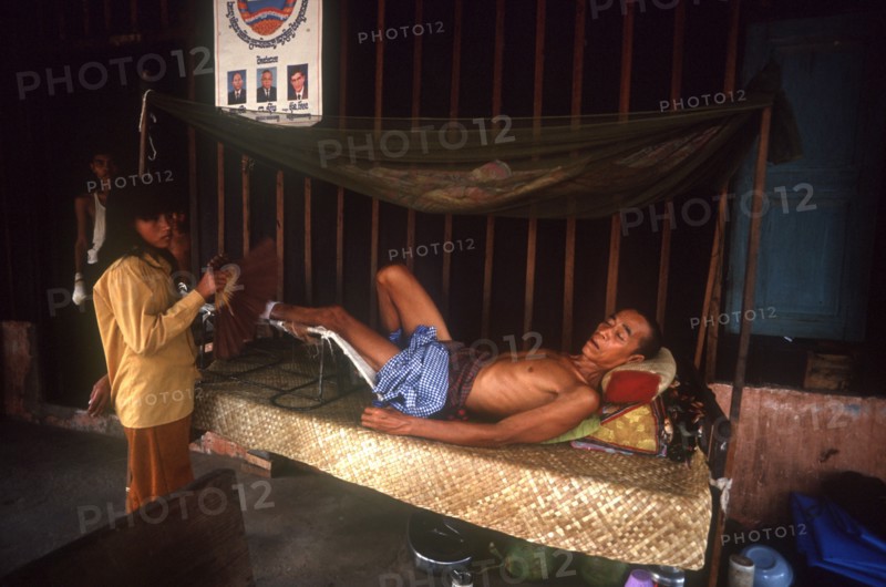 CAMBODIA, Kompong Thom, M.S.F hospital.  Woman fanning male patient lying on a bed.