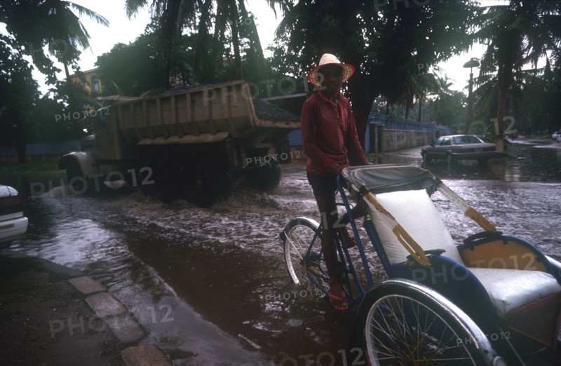CAMBODIA, Phnom Pehn, Rickshaw and truck driving through a flooded street near the Royal Hotel during Monsoon rains.