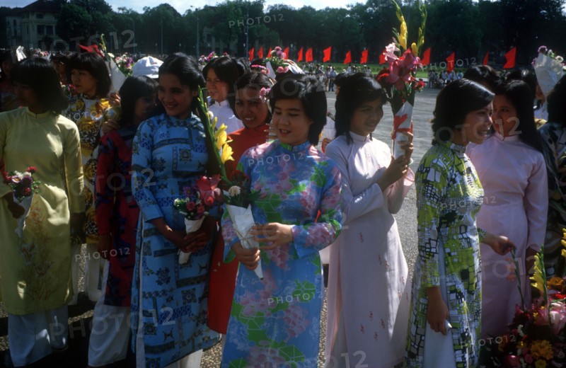 VIETNAM, Hanoi, Young women wearing traditional Cao dai dresses and holding flowers waiting at the finish of a bicycle race.
