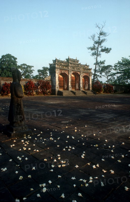 VIETNAM, Hue, Minh Mang Tomb.  View across courtyard scattered with flowers towards ruins with large stone statues on the left.