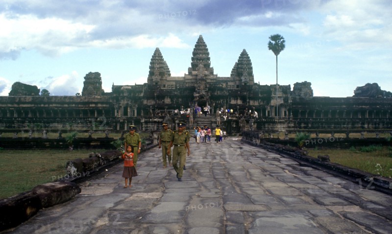 CAMBODIA, Siem Reap, Angkor Wat, "View along wide stone path towards temples and visitors, small girl and temple guards in the foreground."