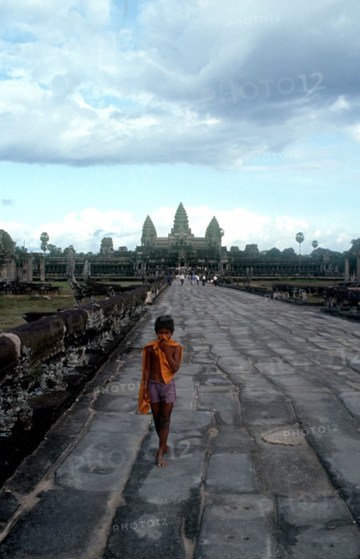 CAMBODIA, Siem Reap, Angkor Wat, Small boy on the stone path leading to the temples which stand against the sky behind.