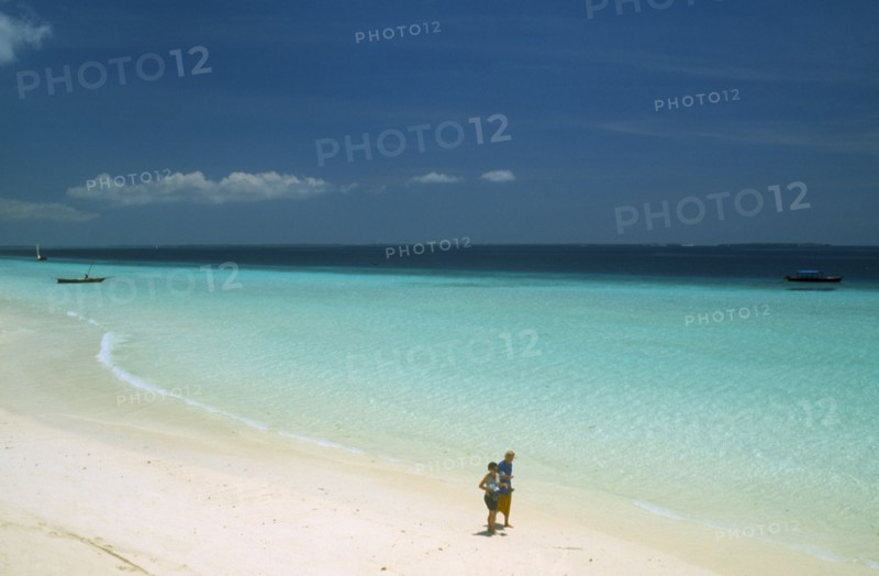 TANZANIA, Zanzibar Island, "Nungwi.  View along beach with white sand and aquamarine sea, towards the skyline.  Couple walking along the shoreline in the foreground. "