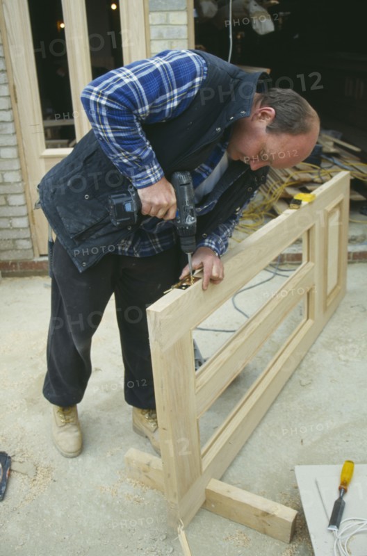 ARCHITECTURE, Construction, Carpentry, Carpenter using power screwdriver to secure hinge to door