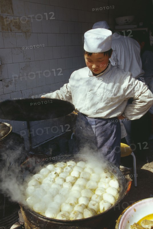 CHINA, Shaanxi Province, Xian, Cook lifting the lid off large dish of frying food.