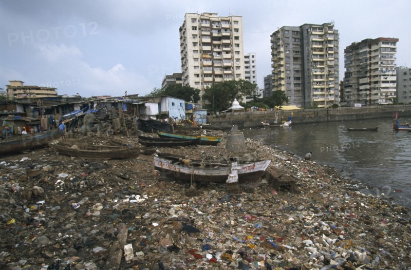 INDIA, Maharashtra, Mumbai , Polluted shoreline covered with rubbish with shanty housing and high-rise buildings behind.