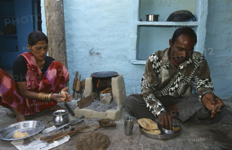 INDIA, Uttar Pradesh, Agra, "Woman cooking chapatis outside over simple, open top stove and serving them to a man sitting on the ground beside her."