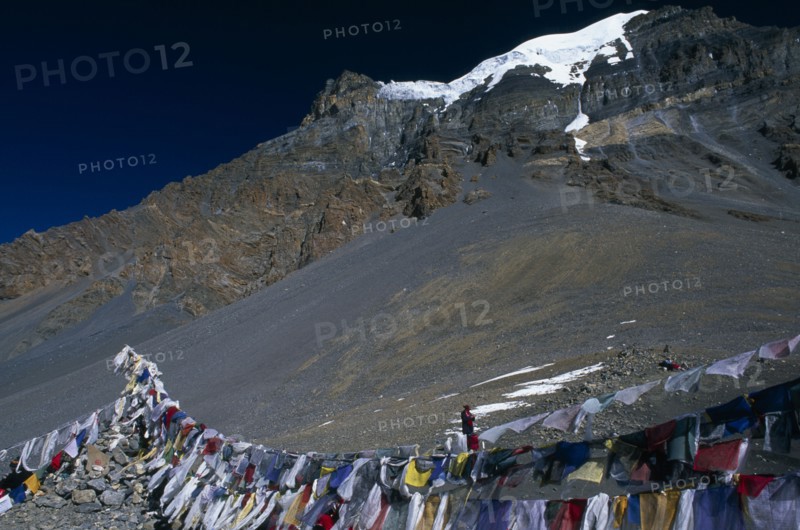 NEPAL, Annapurna Region, Thorung La Pass, Prayer flags hanging at the top of the pass with snow covered mountain peak behind.