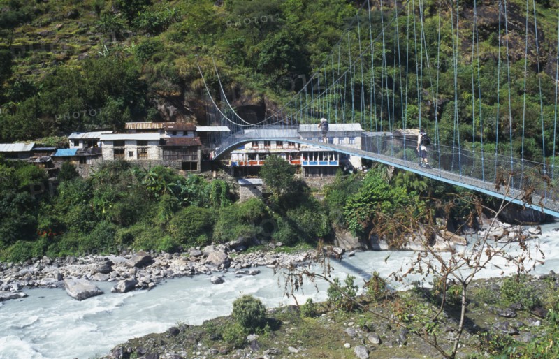 NEPAL, Annapurna Region, Transport, Suspension bridge over fast flowing river near Bhubhule with two trekkers crossing.
