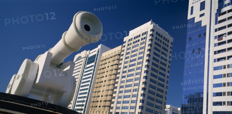 UAE, Abu Dhabi, Al-Ittihad Square.  Angled view of huge sculpture of a cannon with modern high rise buildings behind.