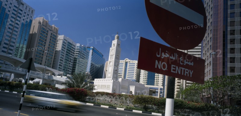 UAE, Abu Dhabi, City centre mosque surrounded by modern high rise buildings with speeding traffic and no entry sign in the foreground.