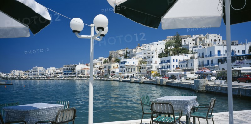 GREECE, Cyclades Islands, Naxos, "Hora.  View from waterside eating area under black and white sun umbrellas, towards white painted town buildings."