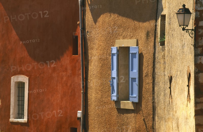 FRANCE, Provence-Cote d’Azur, Vaucluse, Roussillon.  Architectural detail of ochre and terracotta coloured walls with blue window shutter and wall lamp.