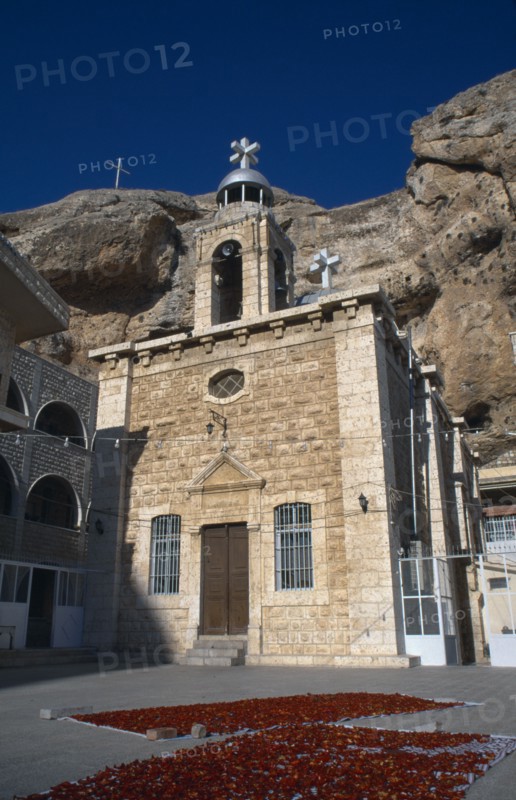 SYRIA, South, Maaloula, "Deir Martalka, the Convent of St Takla.  Exterior and bell tower with flower petals laid out on rugs in the courtyard and steep, eroded cliff face behind."