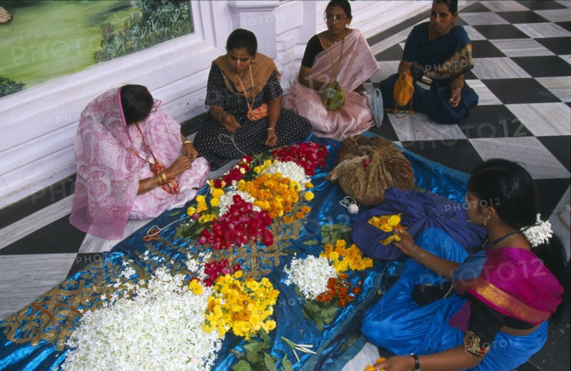 INDIA, Utter Pradesh, Vrindaven, "Women wearing colourful saris making flower garlands, sitting on black and white checked floor."