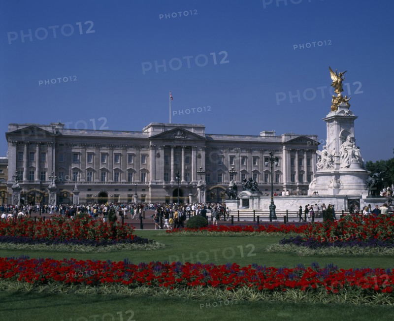 ENGLAND, London, Buckingham Palace and the Victoria Memorial with crowds of visitors outside.  Formal flowerbeds with red and blue flowers in the foreground.