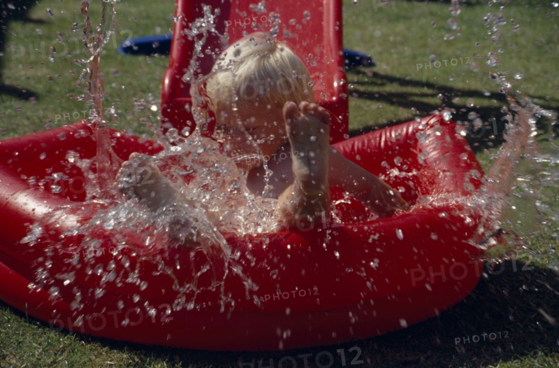 20016668 SPORT Water Paddling Pool Young boy splashing in a red inflatable paddling pool.