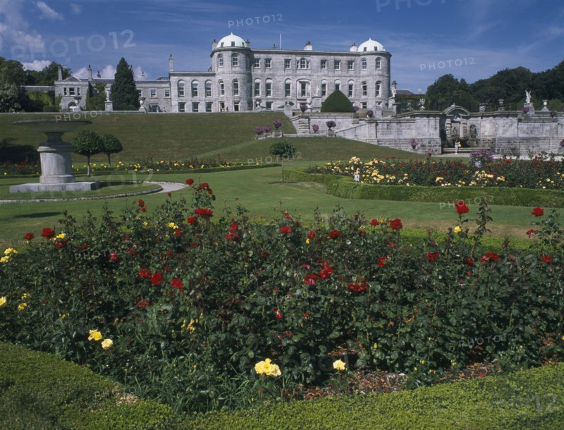 IRELAND, County Wicklow, Powerscourt House, View over formal gardens towards exterior facade.  Flowerbed with red and yellow roses in the immediate foreground.