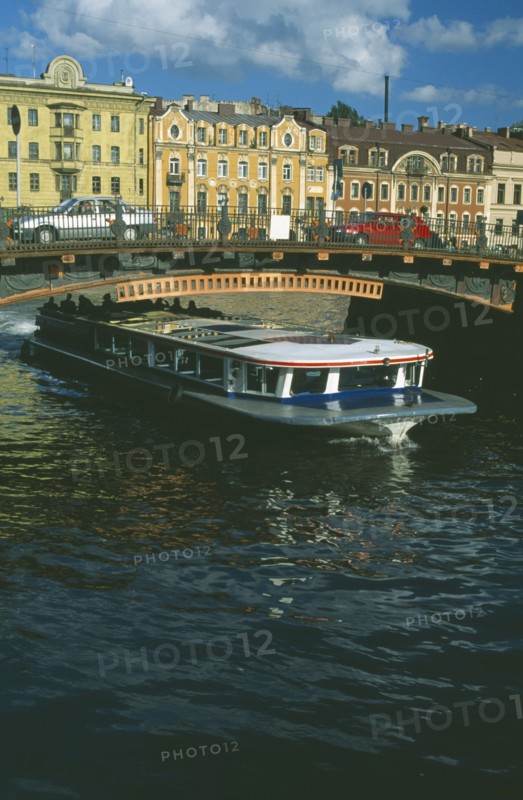 RUSSIA, St Petersburg, Moika Canal with tour boat passing underneath arched bridge with cars crossing and traditional houses behind.