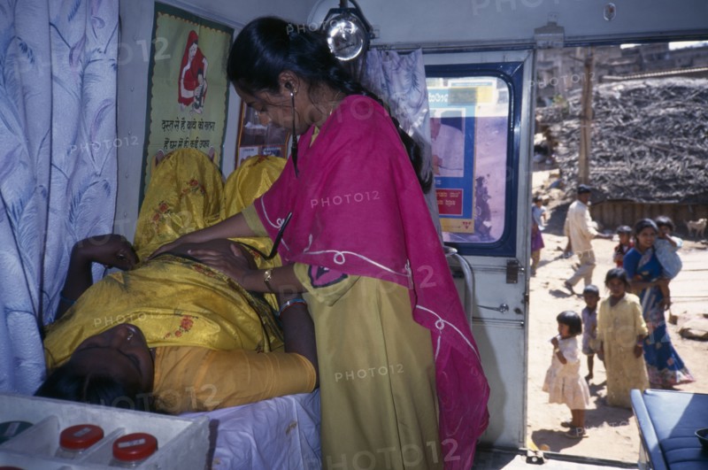 INDIA, Karnataka, Bangalore, Female health worker examining a pregnant woman in a mobile clinic.  Children and woman seen outside through open door.