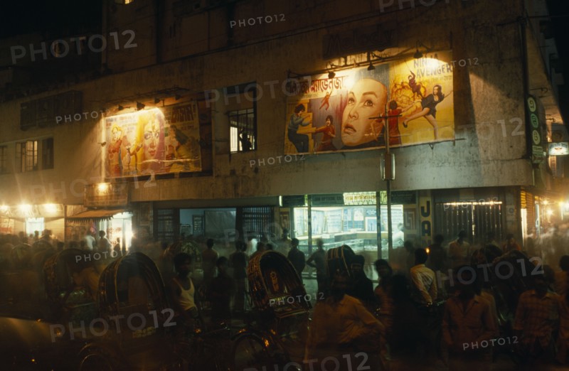 BANGLADESH, Chittagong, "Rickshaw wallahs in front of cinema with posters advertising films above the entrance, illuminated at night."