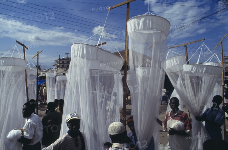 TANZANIA, Dar es Salaam, Mosquito nets for sale at market with men in the foreground and seen through the nets.