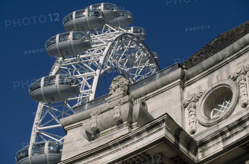 ENGLAND, London, The British Airways London Eye or Millennium Wheel.  Part view seen behind corner of exterior wall of the London Aquarium.