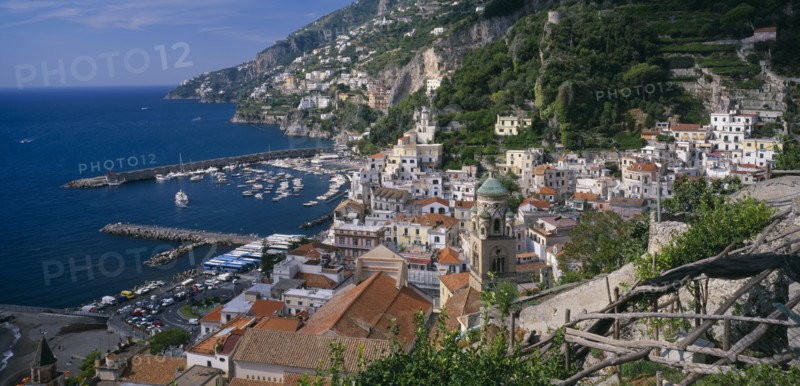ITALY, Campania, Amalfi , View over red tiled roof tops of the town with the Duomo bell tower at its centre towards the harbour and rocky coastline.