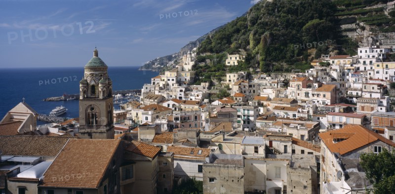 ITALY, Campania, Amalfi , View over red tiled roof tops of the town with the Duomo bell tower on the left and tree covered hillside behind.