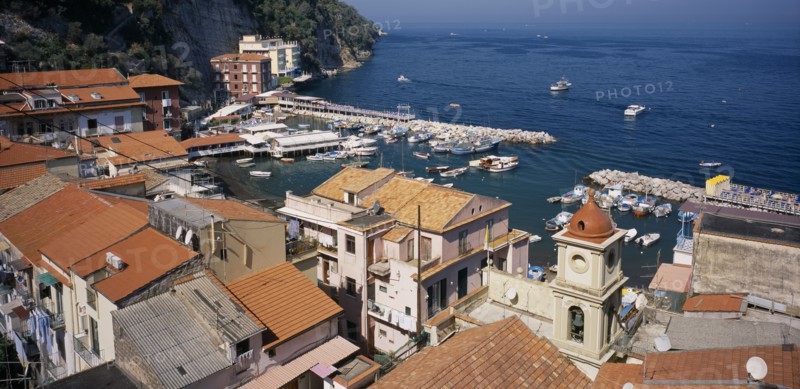 ITALY, Campania, Amalfi Coast, Sorrento.  View over red tiled roof tops and church bell tower towards Marina Grande and moored boats.