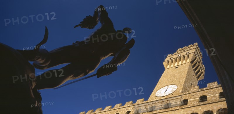 ITALY, Tuscany, Florence, Piazza della Signoria.  Angled view of statue of Perseus with the head of Medusa by Cellini in silhouette with Palazzo Vecchio in sunlight behind.