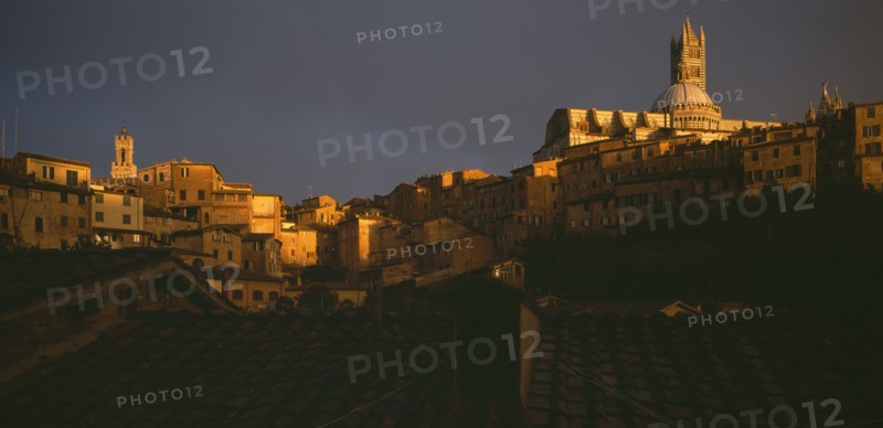 ITALY, Tuscany, Siena, View across the city rooftops towards the Duomo and Campanile in late evening light.