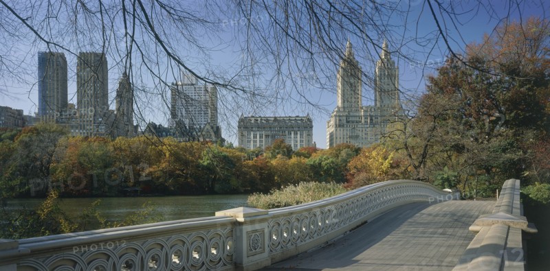 USA, New York State, New York, "Central Park, Bow Bridge.  View over cast iron bridge across lake lined by trees in autumn colours, overlooked by city buildings and the San Remo towers."
