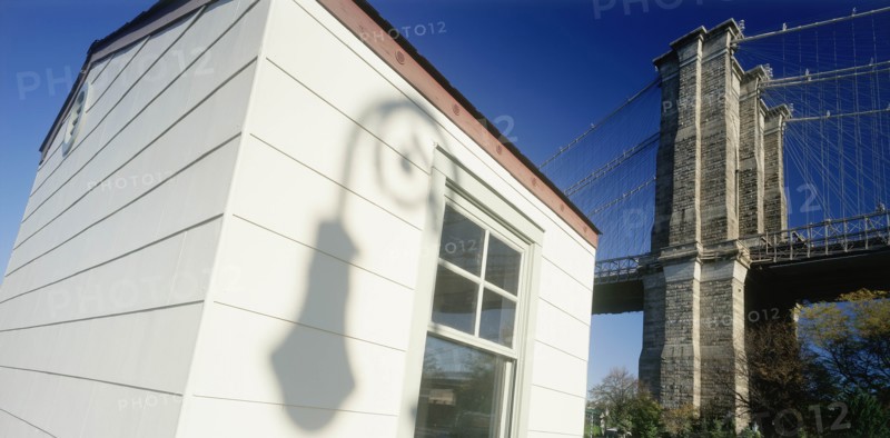 USA, New York , Manhattan, Part view of Brooklyn Bridge with shadow cast by street lamp on exterior wall of white painted building in the foreground.