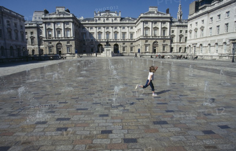 ENGLAND, London, Somerset House and courtyard with rows of small fountains spouting from the ground with a girl running between them.