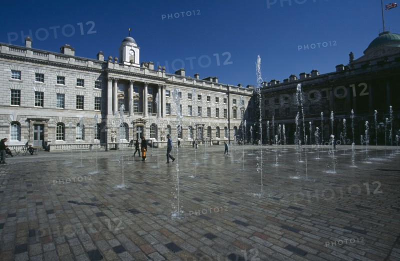 ENGLAND, London, Somerset House and courtyard with rows of fountains spouting high from the ground with people walking between them. Flag flying at half mast in the distance.