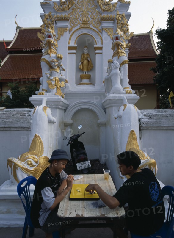 THAILAND, North, Chiang Mai, Wat Mahawan temple with two boys playing go on the pavement below temple wall carvings