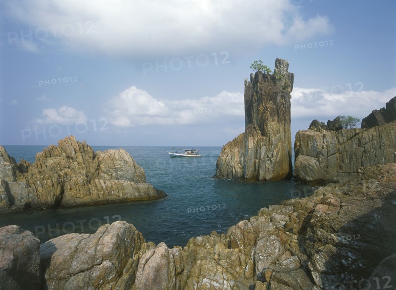 THAILAND, Trat Province, Koh Chang, Laem Chai Chet. Coastal rock formations and cliffs with a small boat  passing by.