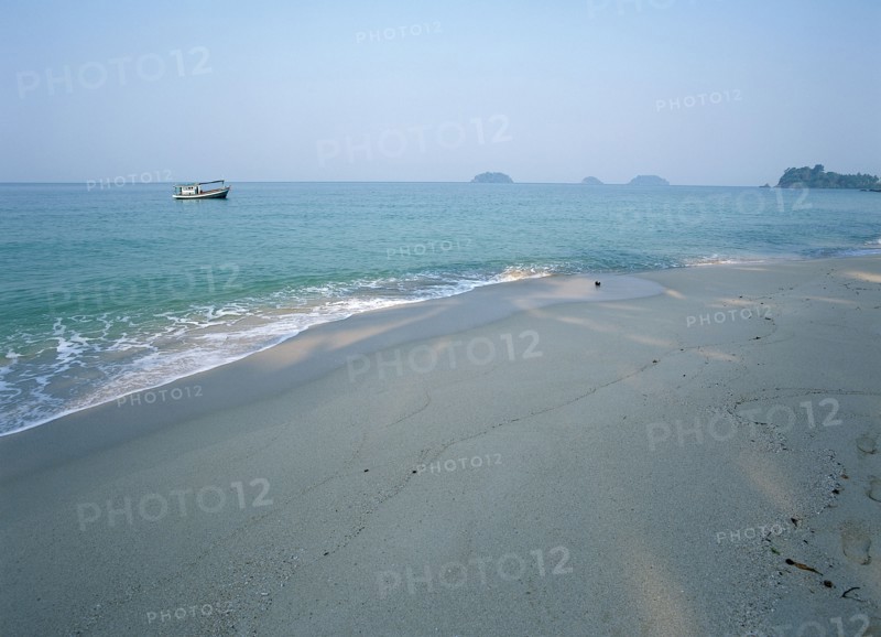 THAILAND, Trat Province, Koh Chang, "Lonley Beach, Aow Bai Lan. Fishing boat seen at anchor off the shaded beach with small islands in the distance."